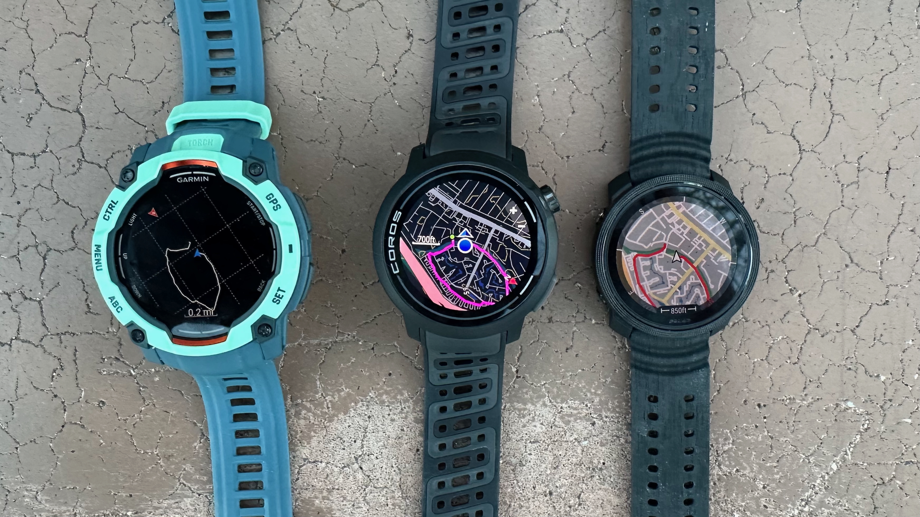 The Garmin Instinct 3 (left), COROS PACE Pro (center), and Polar Vantage M3 (right) showing a mapped activity line; Garmin shows a breadcrumb trail with no offline map details, while the other two have actual streets