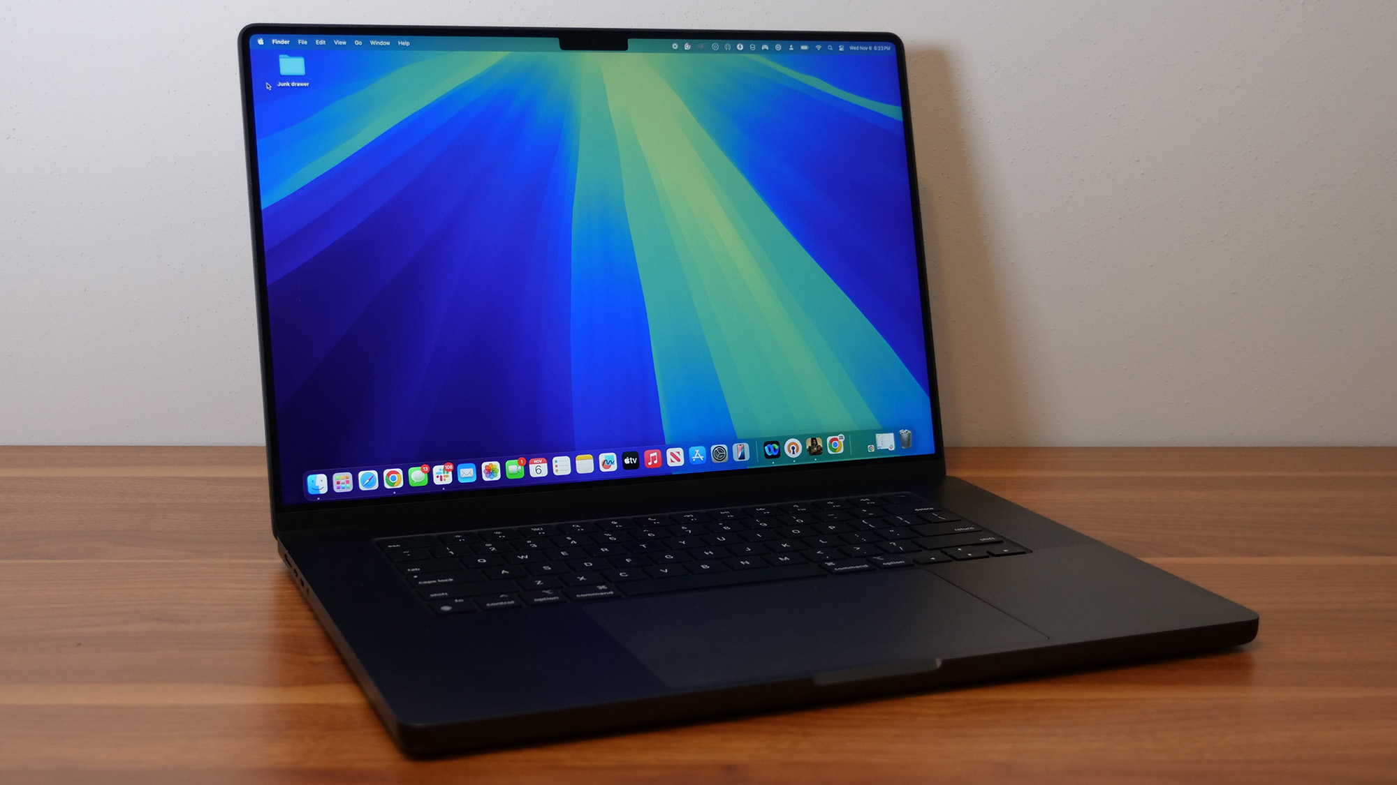 An open and powered on black laptop on a wooden desk against a white wall.