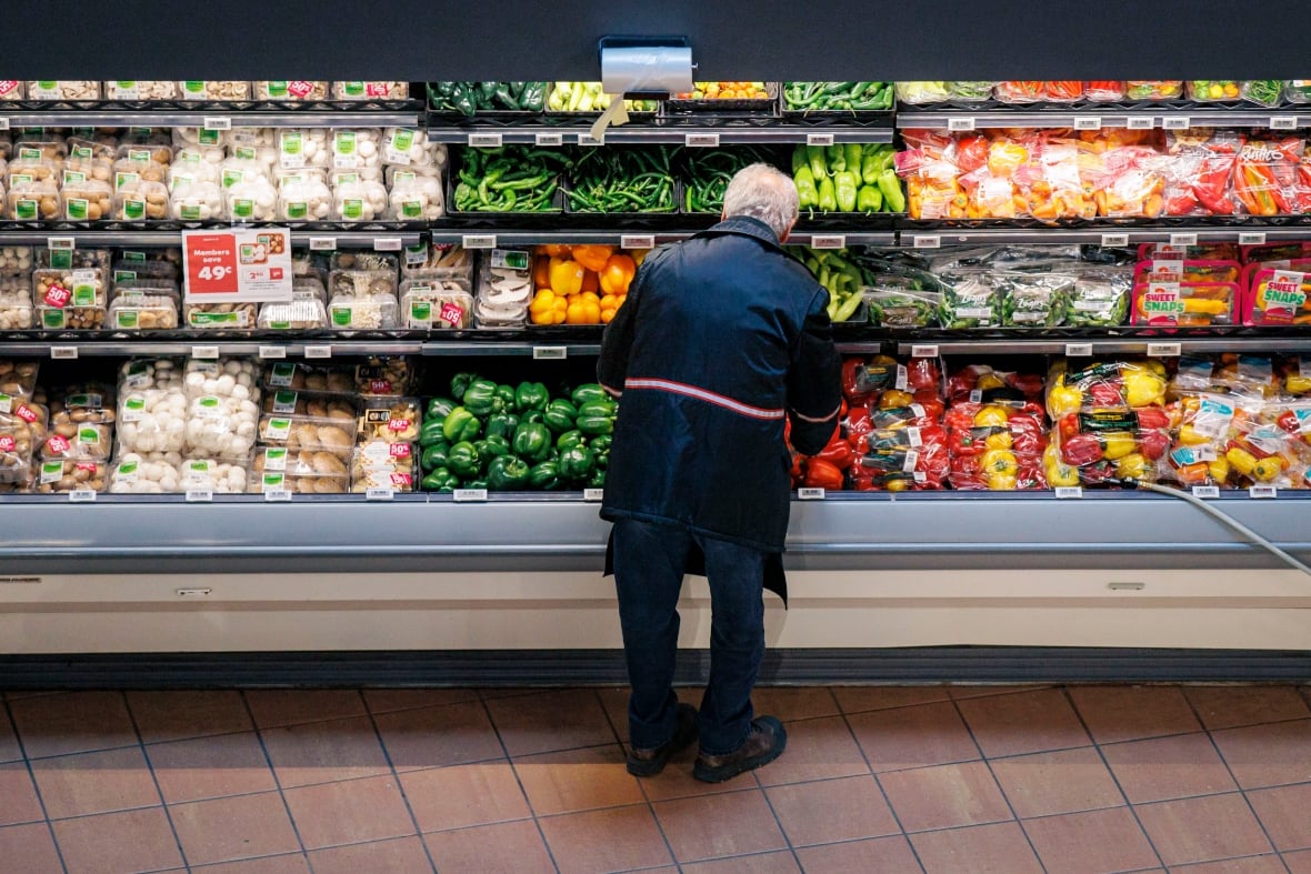 A man looks through the refrigerated vegetable section of a grocery store.